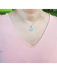 Person wearing a pink top with a necklace featuring a blue opal pendant outdoors.