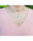 Oval blue-green opal pendant in 14K yellow gold on a woman's neck.