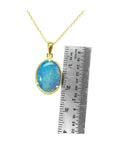 Oval blue-green opal pendant in 14K yellow gold with a ruler for size reference.