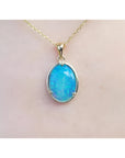 Oval blue-green opal pendant in 14K yellow gold on a delicate chain, worn on skin.