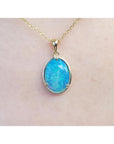 Oval blue-green opal pendant in 14K yellow gold on a delicate chain, worn on skin.