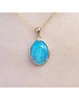 Oval blue-green opal pendant in 14K yellow gold on a delicate chain, worn on skin.