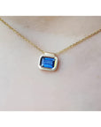 Gold necklace with a blue natural sapphire gemstone bezel set pendant on a woman's neck