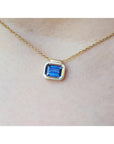 Gold necklace with a blue natural sapphire gemstone bezel set pendant on a woman's neck