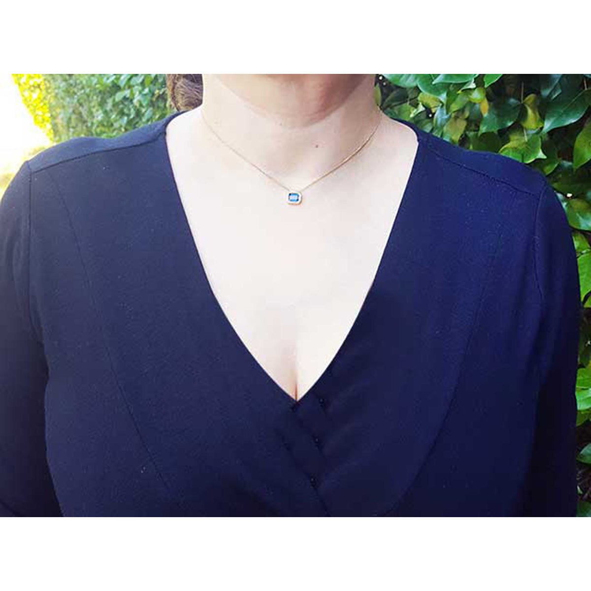 Lady wearing a deep V-neck navy blue top with a blue sapphire necklace against a green leafy background