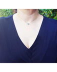 Lady wearing a deep V-neck navy blue top with a blue sapphire necklace against a green leafy background