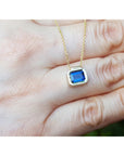Yellow gold necklace with a blue natural sapphire bezel set pendant held in a hand.