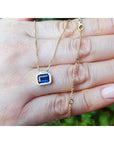 Gold necklace with a blue natural sapphire pendant and chain held in a hand against a blurred natural background