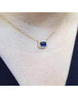 Gold necklace with a blue sapphire gemstone pendant on a person wearing a dark top.