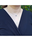 Woman wearing a 14K yellow gold necklace with an east-west emerald cut blue sapphire and diamond pendant.