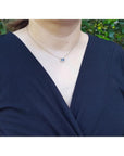 Woman wearing a 14K yellow gold necklace with an east-west emerald cut blue sapphire and diamond pendant.