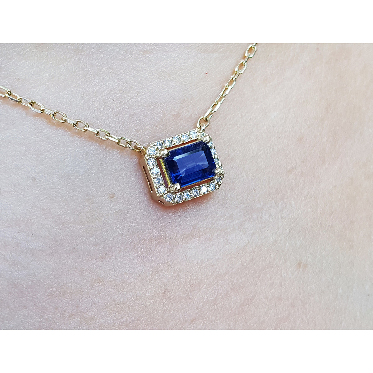Gold necklace with a blue sapphire gemstone pendant on a light background