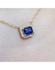 Gold necklace with a blue sapphire gemstone pendant on a light background