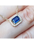 Displaying on fingers top view of a blue sapphire necklace emerald cut halo diamonds in 14k yellow gold.