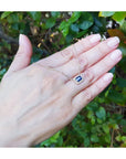 Hand showcasing a gold necklace with a blue sapphire gemstone against a green leafy background