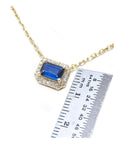 Gold necklace with a blue sapphire gemstone pendant next to a ruler for scale on a white background
