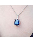 Blue cushion cut sapphire gemstone pendant on a chain against a skin background