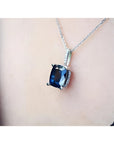 4.11 ct deep blue cushion cut sapphire pendant in 14K white gold, worn on a neck.
