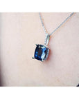 4.11 ct deep blue cushion cut sapphire pendant in 14K white gold, worn on a neck.