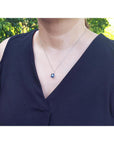 Lady wearing a dark blue top with a necklace featuring a blue sapphire pendant, outdoors.