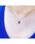 14k gold necklace with a rectangular blue sapphire pendant and three accent diamonds on a person's neck.
