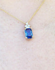 Gold necklace with a blue genuine sapphire pendant on a light beige skin background.