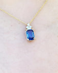 Gold necklace with a blue genuine sapphire pendant on a light beige skin background.