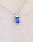 Gold necklace with a blue genuine sapphire pendant on a light beige skin background.