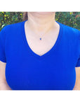 Woman wearing a 14k gold necklace with an emerald-cut blue sapphire pendant and diamond accents.