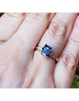 A 14k yellow gold ring with a blue natural sapphire rich medium-dark hue, flanked by two tapered baguette natural diamonds on a person's finger.
