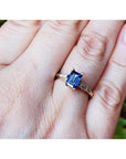 A 14k yellow gold ring with a blue natural sapphire rich medium-dark hue, flanked by two tapered baguette natural diamonds on a person's finger.