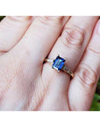 Gold ring with a blue natural sapphire on a person's finger against a natural background