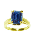 A women’s blue sapphire solitaire ring featuring a deep blue, rectangular emerald-cut sapphire set in 14k yellow gold.