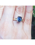 Gold ring with a blue sapphire gemstone on a hand against a blurred green background