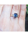 Emerald cut 3.13 ct. deep blue sapphire solitaire ring in 14K yellow gold on a hand.