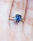 Blue sapphire solitaire ring for women emerald cut 14k yellow gold, on a person's finger.