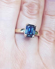 Blue sapphire solitaire ring for women emerald cut 14k yellow gold, on a person's finger.