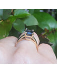Yellow gold ring with a blue sapphire on a hand against a green leafy background