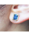Close-up of an ear wearing a blue sapphire earring with gold setting.