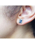 Emerald cut blue sapphire halo diamond stud earring in 14K yellow gold on an ear.