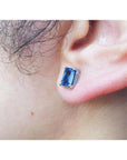 Emerald cut deep blue sapphire stud earring in 14K white gold worn on an ear.