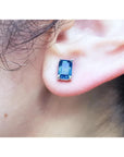 Emerald cut deep blue sapphire stud earring in 14K white gold on an ear.