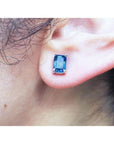 Emerald cut deep blue sapphire stud earring in 14K white gold on an ear.