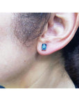 Emerald cut deep blue sapphire solitaire stud earring in 14K white gold on an ear.