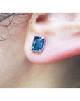 Blue natural sapphire earring set in 14k white gold on a person's ear.