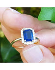 Women's 14k yellow gold ring with emerald-cut blue sapphire and halo diamonds.