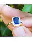 Women's 14k yellow gold ring with emerald-cut blue sapphire and halo diamonds.