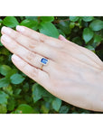 Women's 14k yellow gold ring with emerald cut blue sapphire and diamond halo on a hand.
