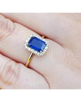 Women's 14k yellow gold ring with emerald-cut blue sapphire and diamond halo.