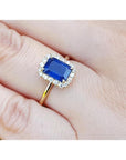 Women's 14k yellow gold ring with emerald-cut blue sapphire and diamond halo.
